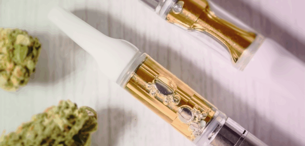 Macro shot of golden cannabis oil cartridges alongside dried flower on a light surface.