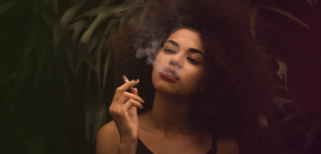 A woman smokes a joint in a dimly lit environment.
