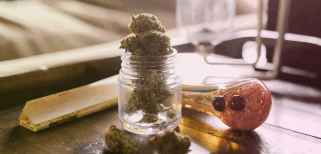 A jar filled with cannabis nugs with a pipe next to it.
