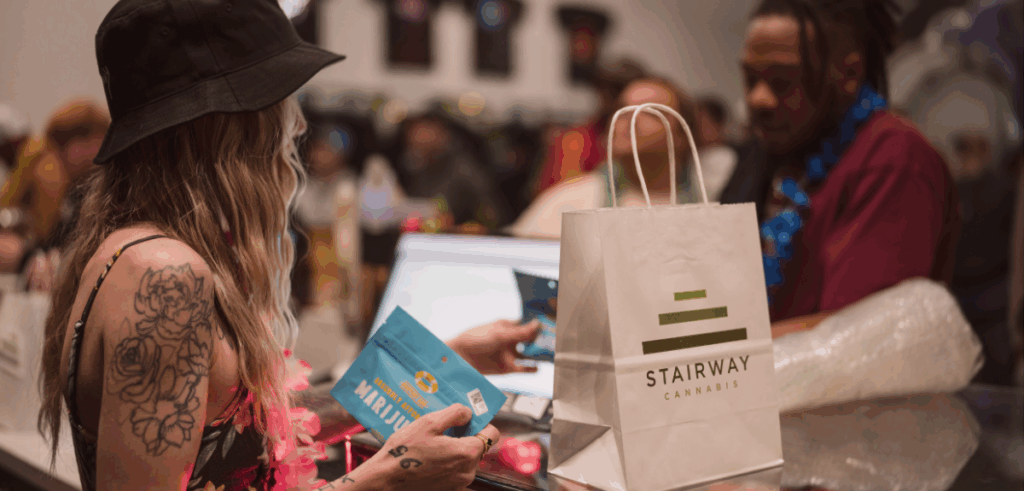 Stairway Cannabis employee handing items to a first time dispensary customer at a checkout counter with a Stairway Cannabis bag.