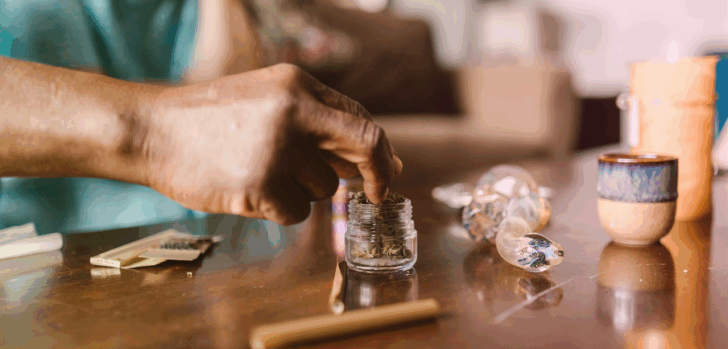 A close up of a black man's hand reaching into a jar of cannabis flower.
