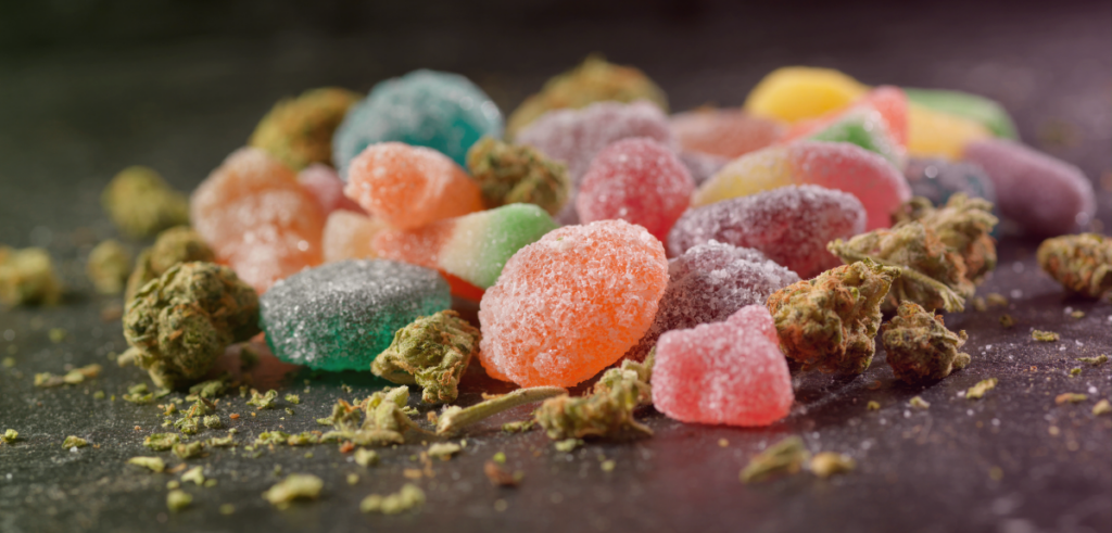 Cannabis nugs and gummies in a pile on a grey surface.