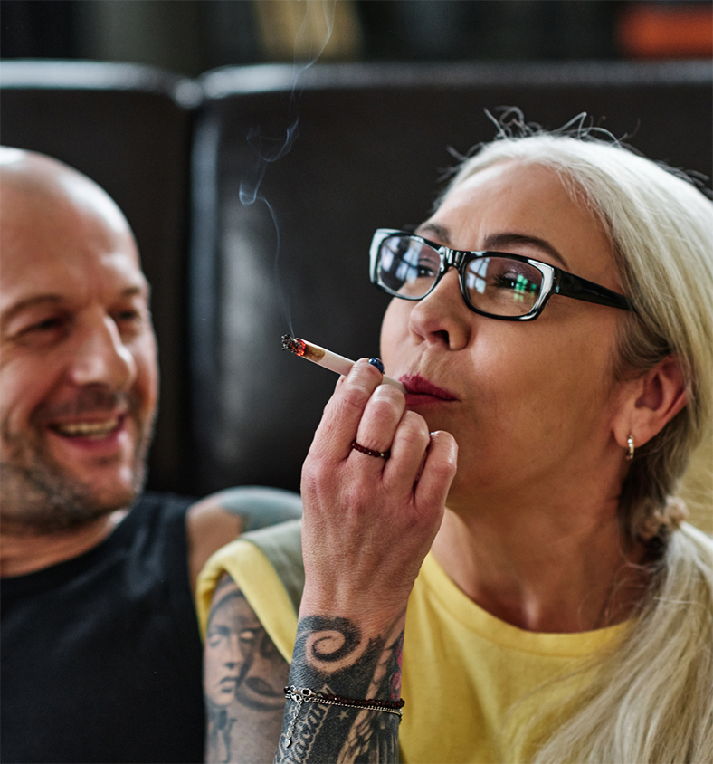 A man laughs as a woman wearing a yellow shirt takes a puff on a joint.