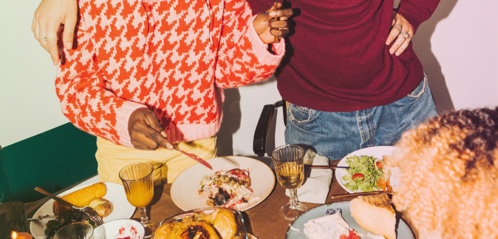 A cozy gathering at a dinner table with people sharing a meal, featuring various dishes, salads, and drinks.