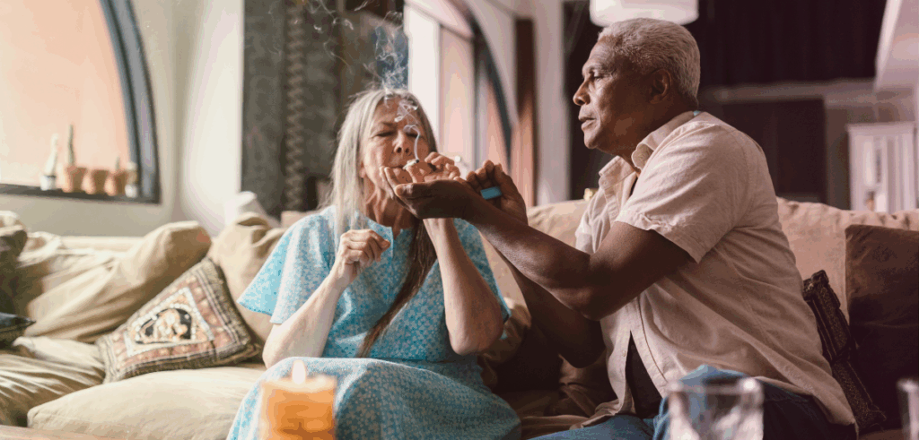 An older couple shares a relaxed moment on the couch, lighting a joint in a cozy living room.